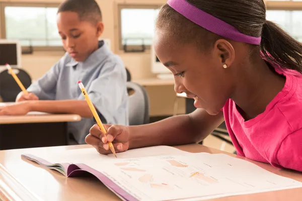 Girl practices handwriting in a workbook at a desk