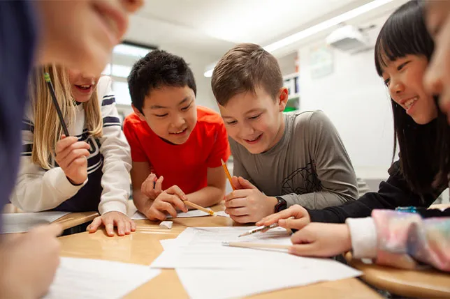 Students gathered around a table sharing pages of their writing