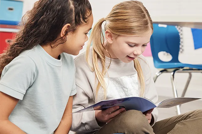 Two students looking at a picture book together in a classroom
