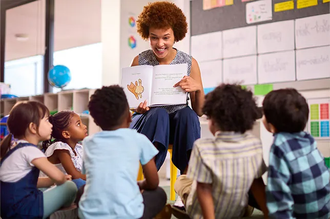Teacher reading a book aloud to the class, pointing to page