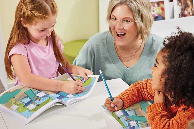 Teacher sitting next to students who are writing in notebooks
