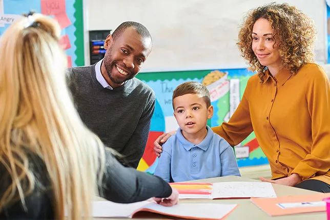 Smiling parents and child seated at a classroom table with teacher during family conference