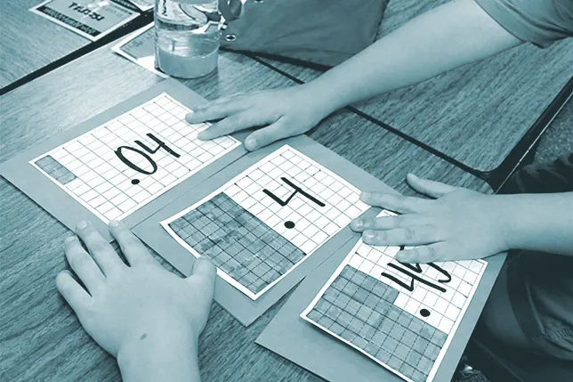 Two students collaborate to order images of .04, .4, and .45 on a number line at a table