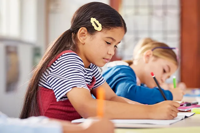 Students practice handwriting at desks in classroom