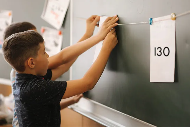 Two students hang numbers on a string at the board