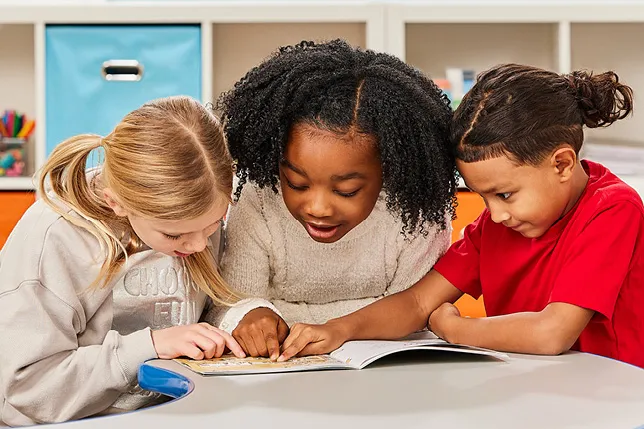Three students huddled around a book reading and pointing at page