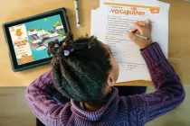 Student completing vocabulary page of Spelling Connections lesson with a spelling quest visible on nearby tablet