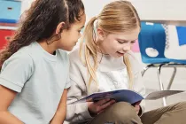 Two students looking at a picture book together in a classroom